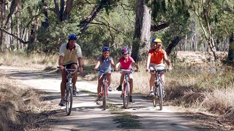 A family of four riding push bikes along a dirt road